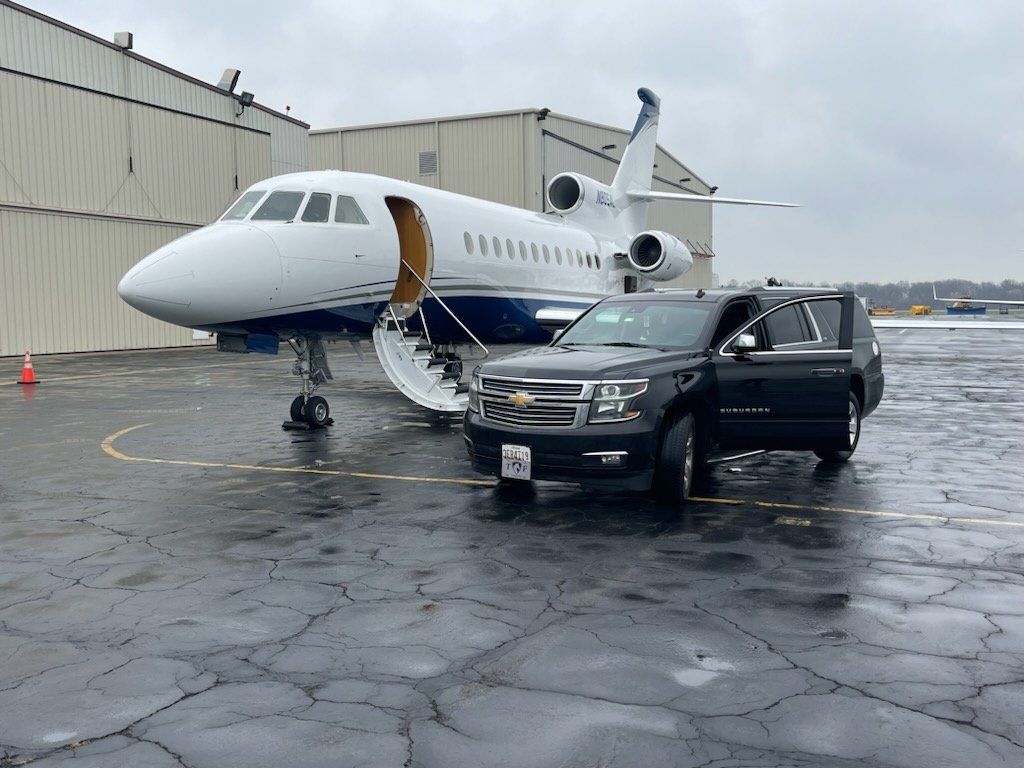 A car is parked next to a private jet at an airport.