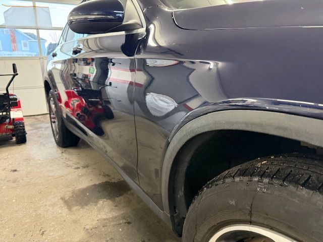 Dark blue car parked inside a garage, snow blower visible in the background. | Big n' Littles Auto Body