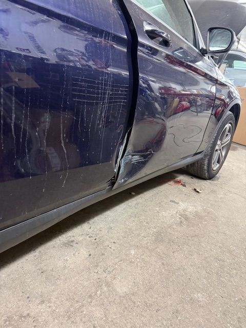 Damaged blue car door, dented and scratched, in a repair shop setting. | Big n' Littles Auto Body