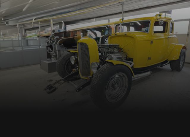 A yellow hot rod coupe parked inside a garage workshop. | Big n' Littles Auto Body