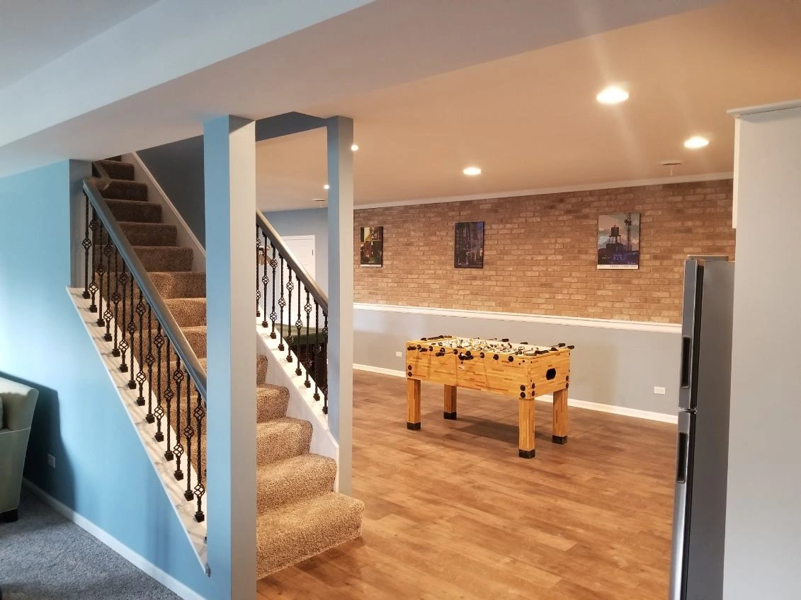 Basement rec room with staircase, foosball table, brick accent wall, and hardwood floor