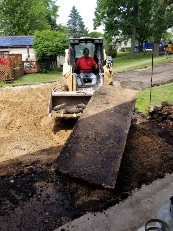Bulldozer pushing gravel over a torn-up road near houses and trees