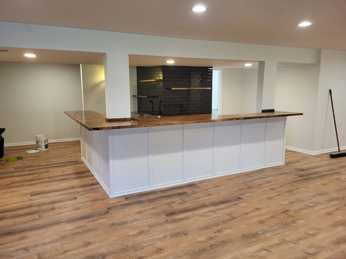 Empty room with wood floors and a white kitchen island in a partially finished basement.