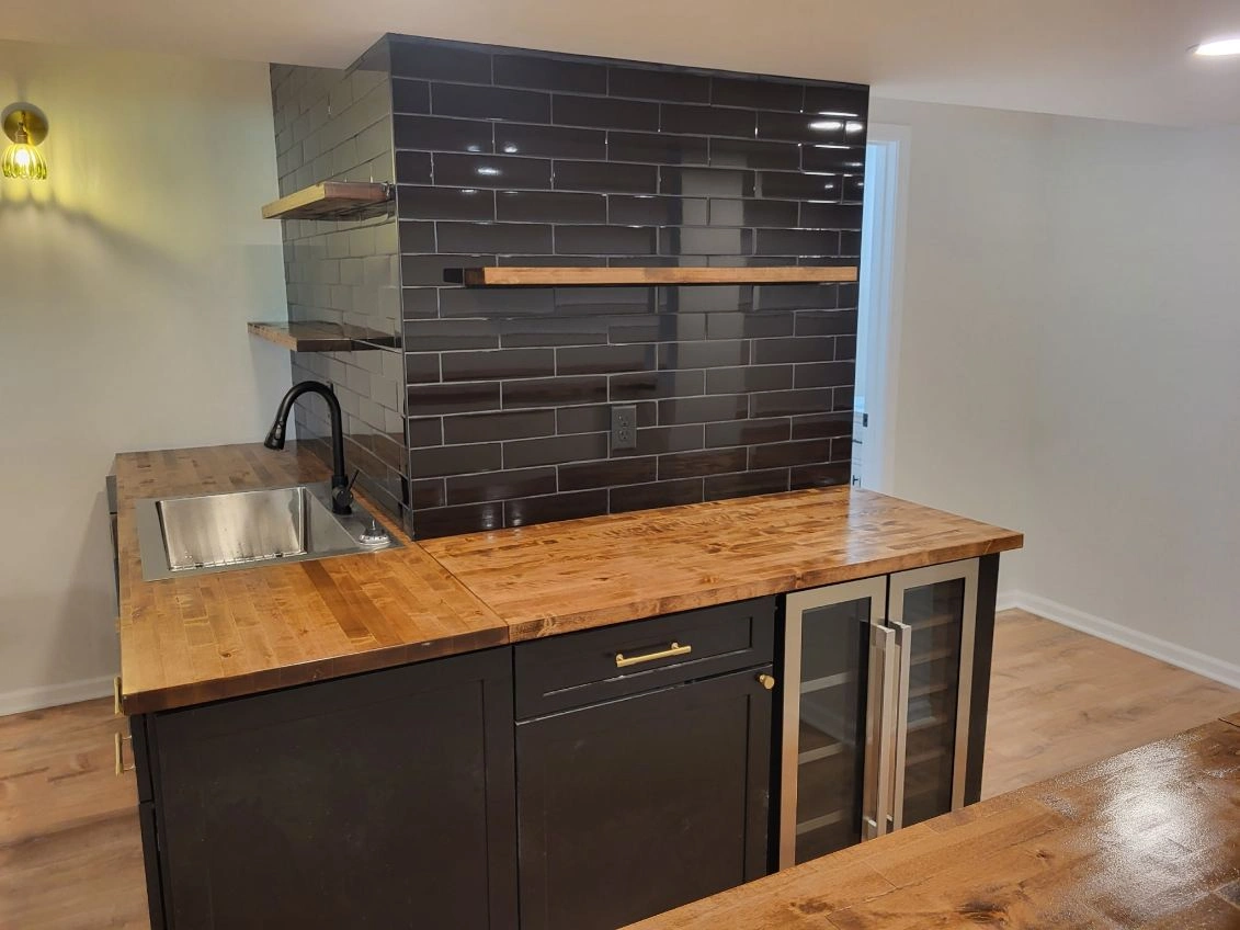 Modern kitchen with black tile backsplash, wood countertops, sink, and bar seating.
