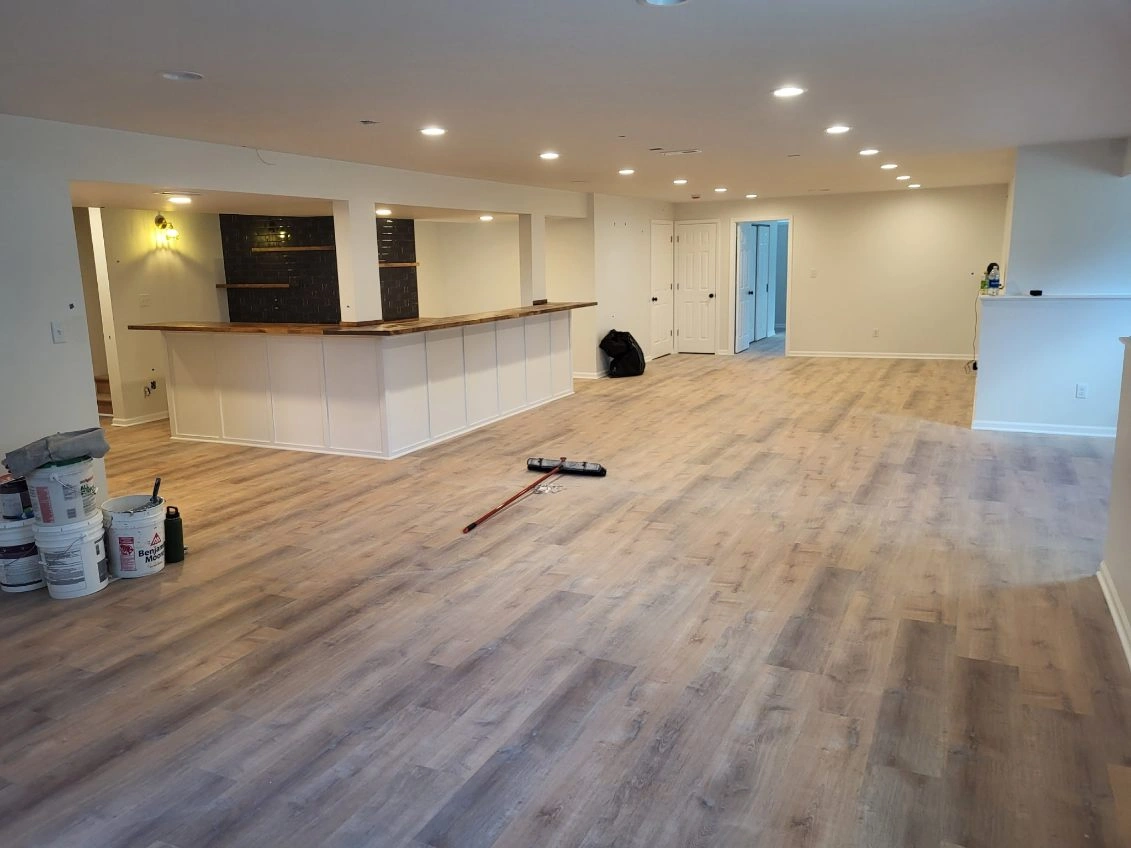 Empty open-plan room with wood flooring, white kitchen island, recessed lights, and a blue door.