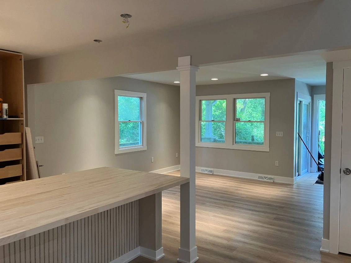 Empty modern living space with wood floors, white walls, windows, and a kitchen island