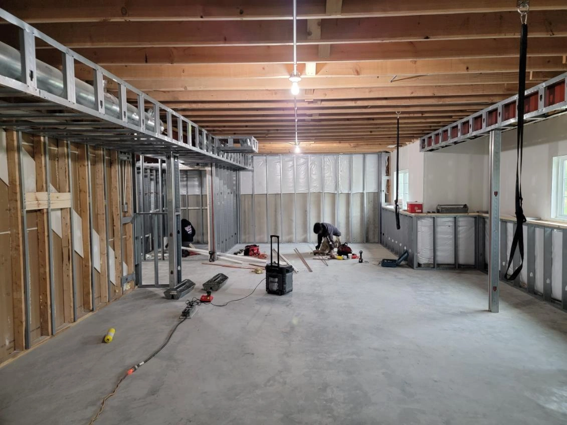 Unfinished basement with exposed framing, concrete floor, tools, and construction materials scattered around.