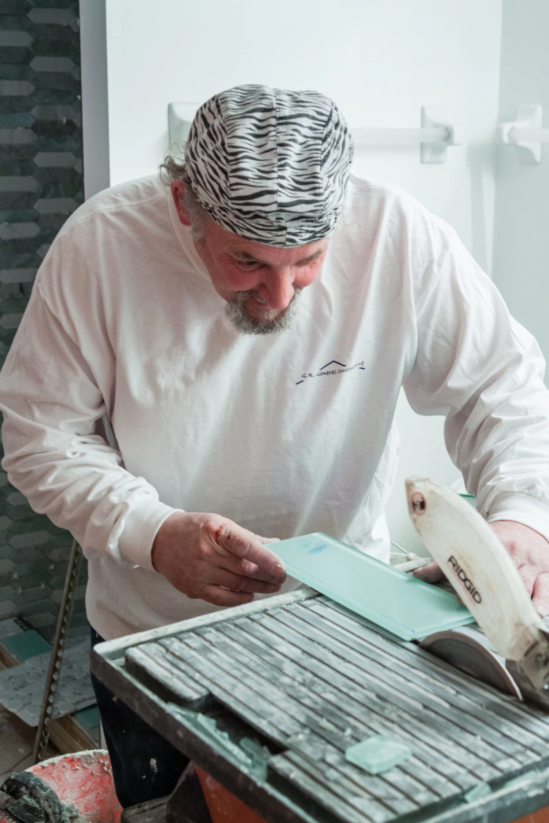 Person in white clothing using a tool on a worktable with slats in a workshop