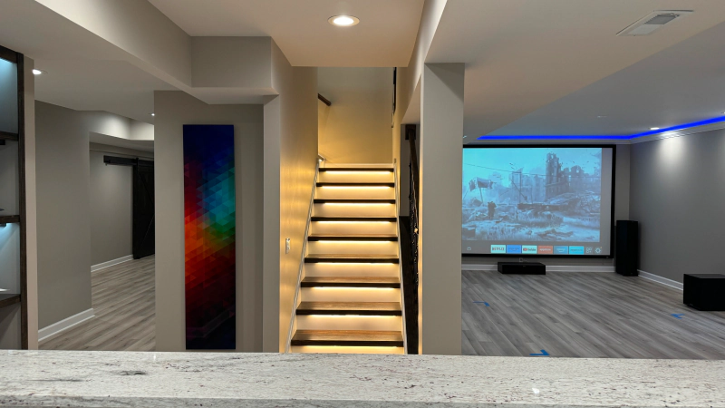 Modern basement home theater with lit staircase, large projector screen, and blue accent lighting