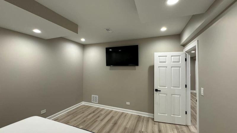 Modern empty bedroom with gray walls, wood-look floor, wall-mounted TV, and white closet door