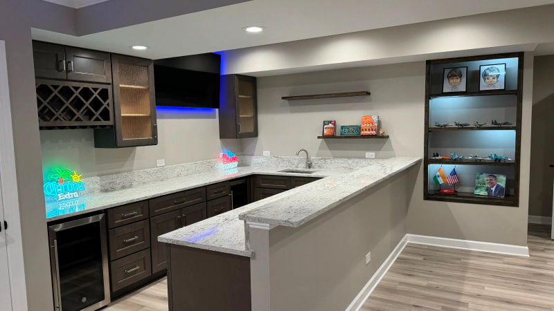 Modern basement kitchen with dark cabinets, marble island, wine rack, and built-in wall shelves.