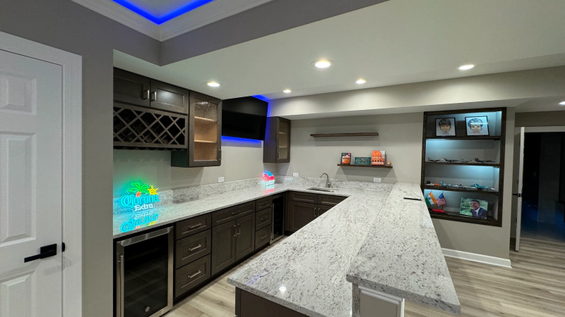 Modern kitchen with dark cabinets, white marble island, recessed lighting, and built-in wine storage.