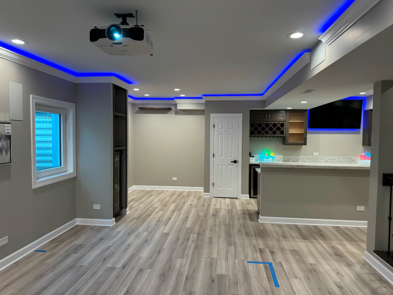 Modern open-plan living room with gray walls, blue LED ceiling lights, and a kitchen bar area