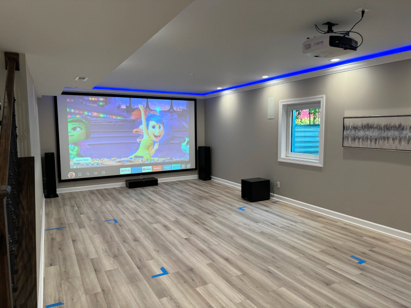 Empty room with projector screen, blue LED ceiling lights, and a wood-look floor marked with tape.