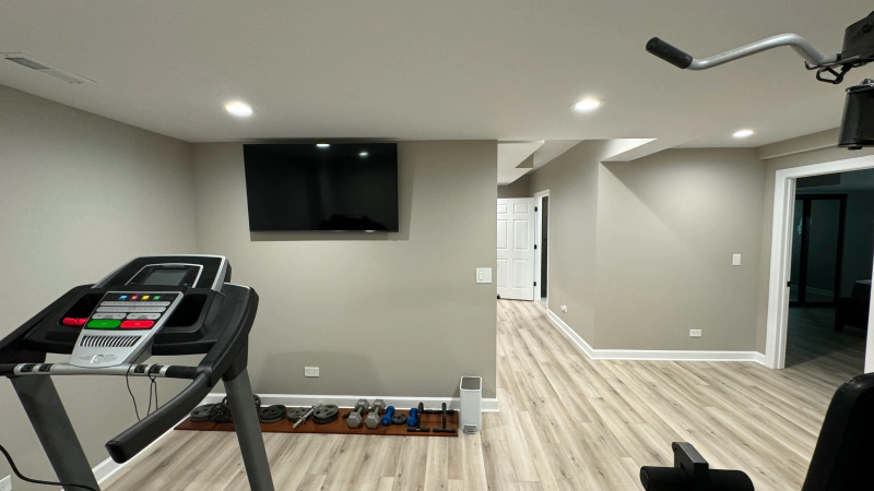 Modern home gym with treadmill, wall TV, and light wood flooring