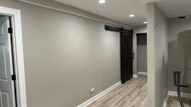 Empty modern hallway with gray walls, wood floor, recessed lights, and a black barn-style door.