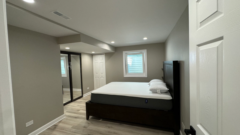 Modern bedroom with gray walls, a bed, mirrored closet doors, and a window with blinds.