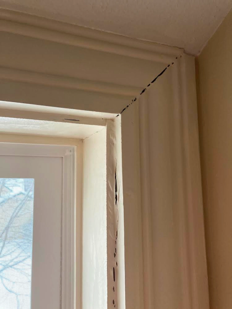 Close-up of a beige window frame with peeling paint near the top corner.