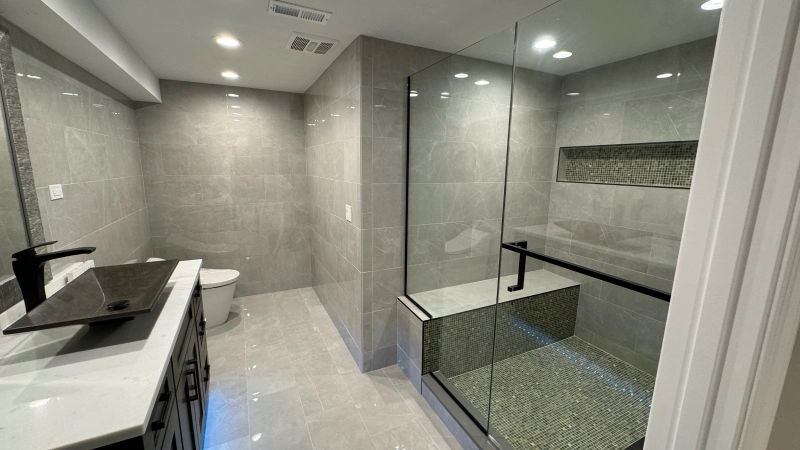 Modern gray-tiled bathroom with a vanity sink, mirror, and glass-enclosed shower area