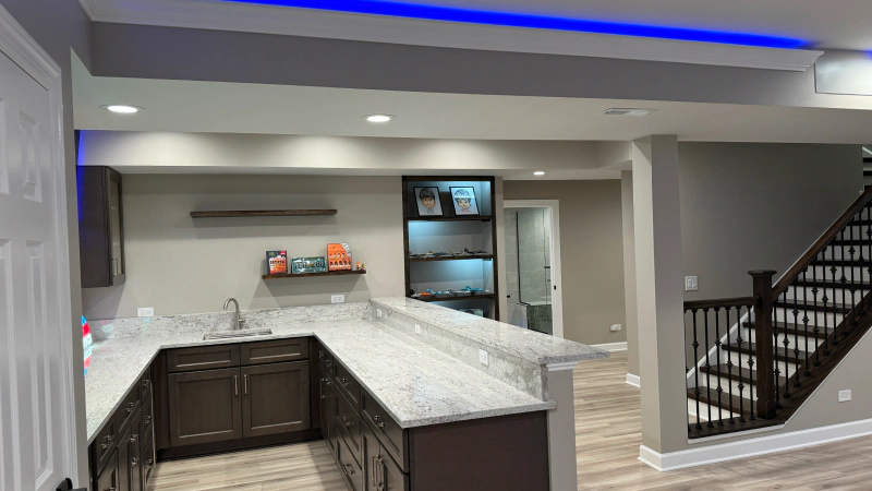 Modern kitchen with gray cabinets, white countertops, built-in refrigerator, and blue ceiling accent lighting