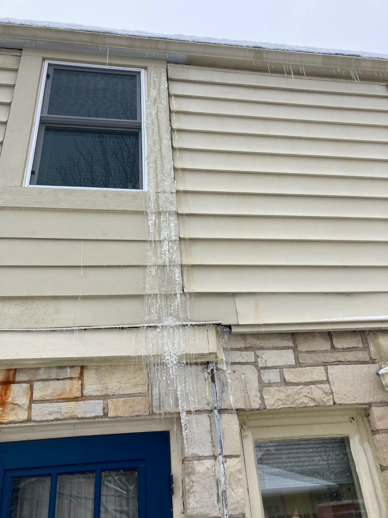 Water pouring down the siding of a house from the roof near a second-floor window