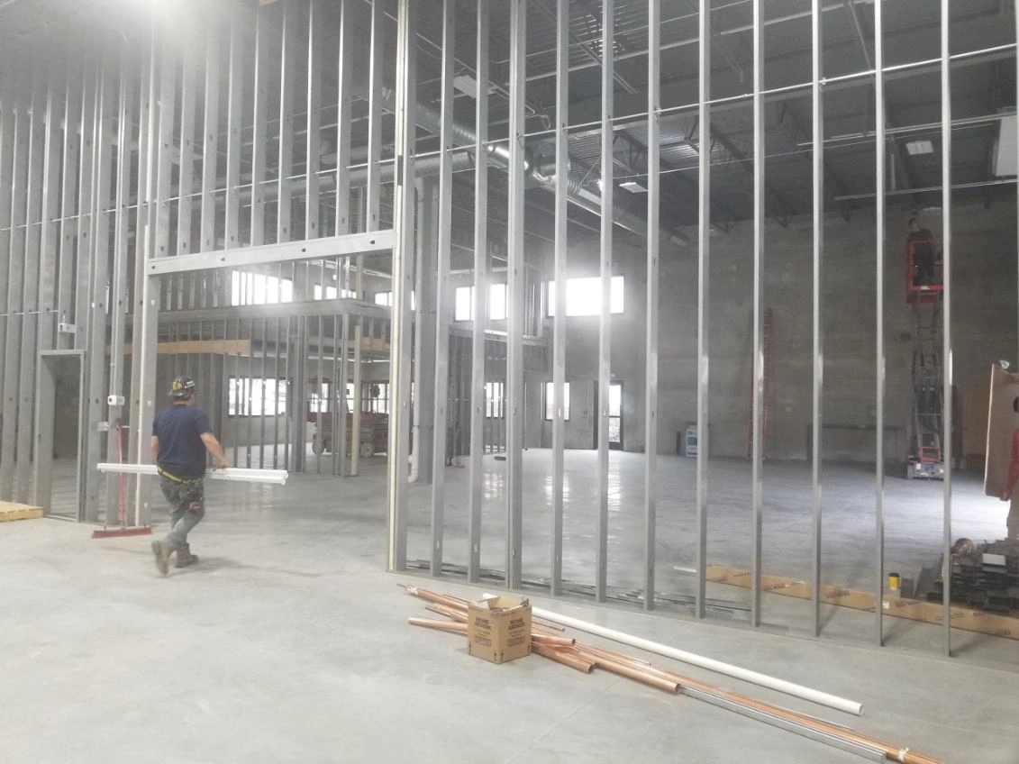 Construction site with metal wall framing and a worker walking on a concrete floor inside a large unfinished building