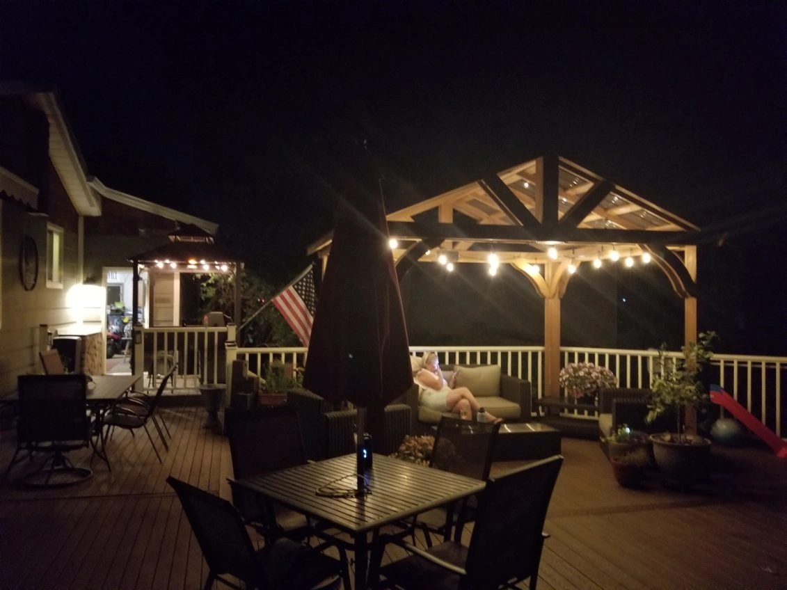 Outdoor deck at night with patio tables, chairs, string lights, and a lit gazebo.
