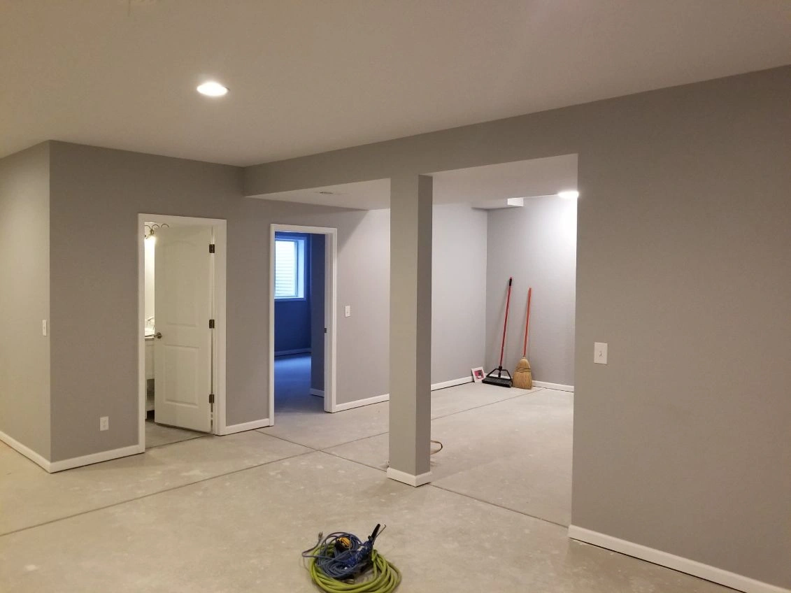 Empty unfinished room with gray walls, beige carpet, open doorway, and cleaning tools on the floor