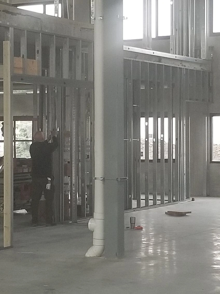 Construction site interior with metal framing, concrete floor, and a worker near a doorway
