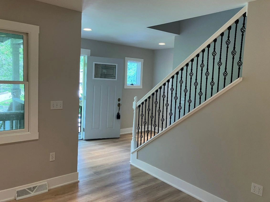 Empty foyer with staircase, light wood floors, and white walls in a bright home interior.