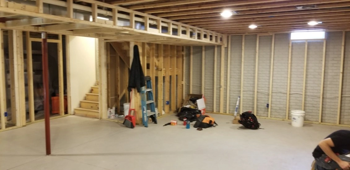 Unfinished basement with exposed framing, stairs, tools, and construction materials scattered on the floor