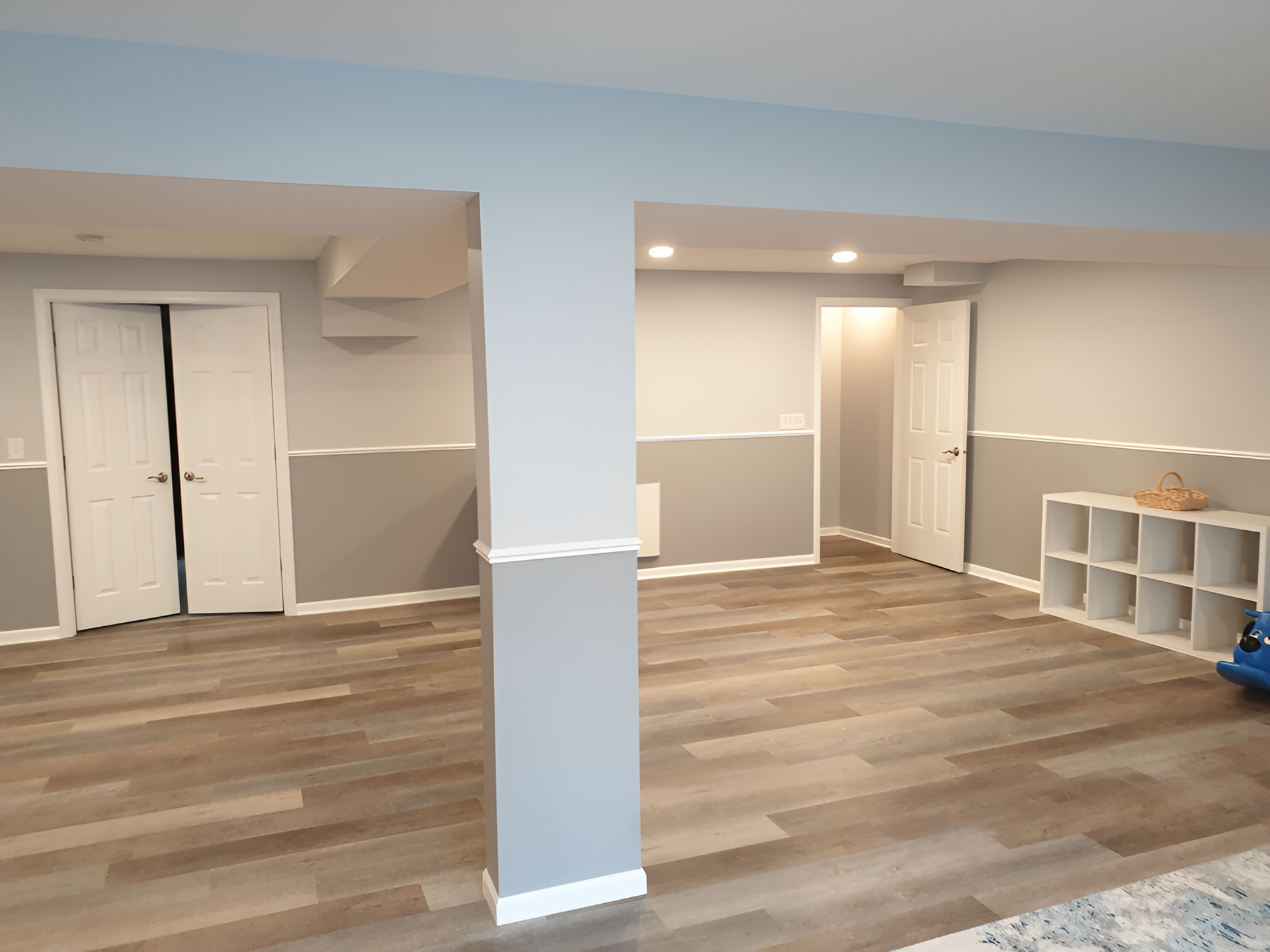 Empty basement room with wood-look floors, gray walls, recessed lights, and white cubby shelves