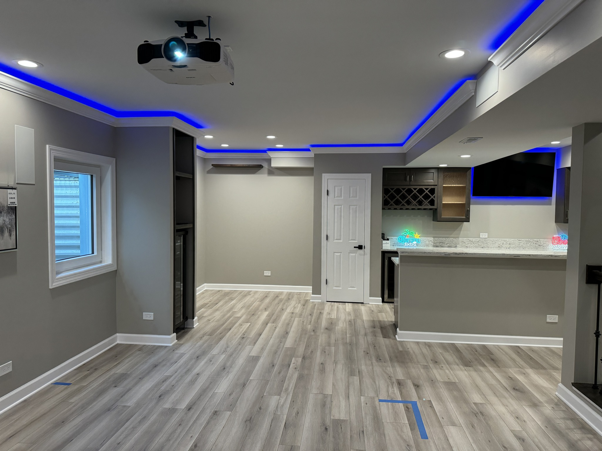 Empty gray living room with blue LED ceiling lights, wood-look floor, and open kitchen bar area