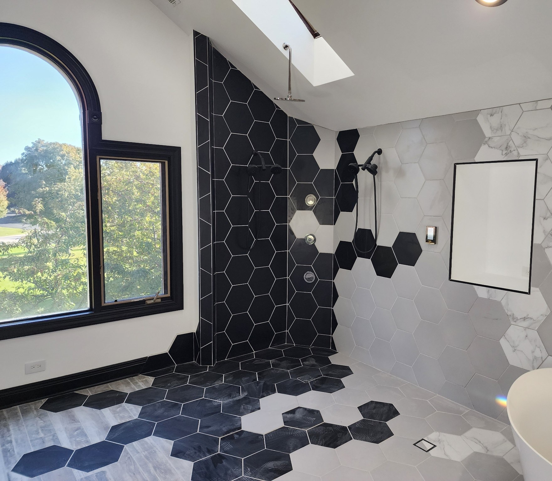 Modern bathroom with black hex tile floor, gray walls, large arched window, and white sink.