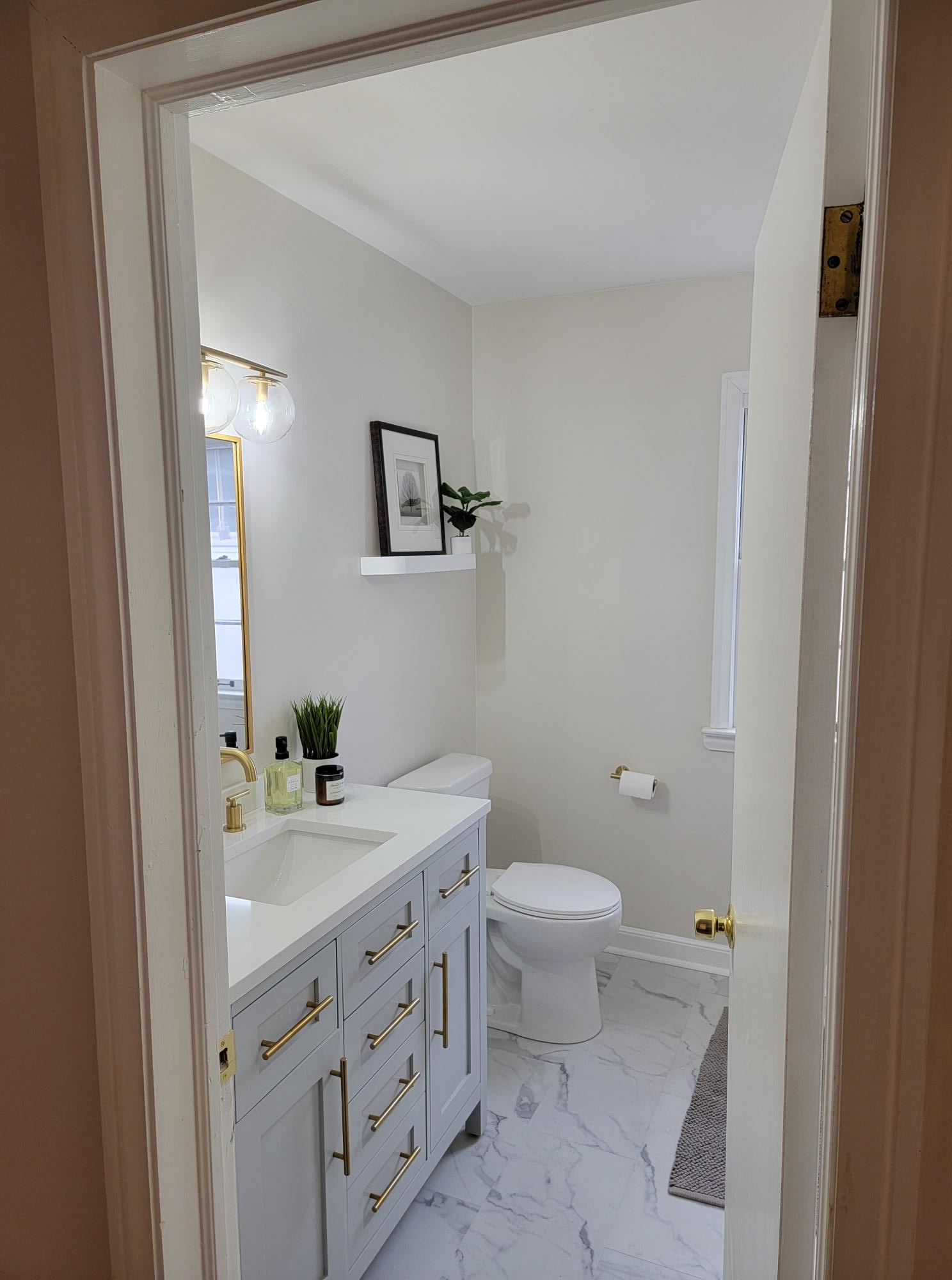 Bright white bathroom with vanity, toilet, mirror, wall shelf, and window