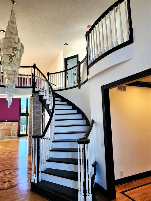 Spiral staircase in a bright modern foyer with dark railings and hardwood floors