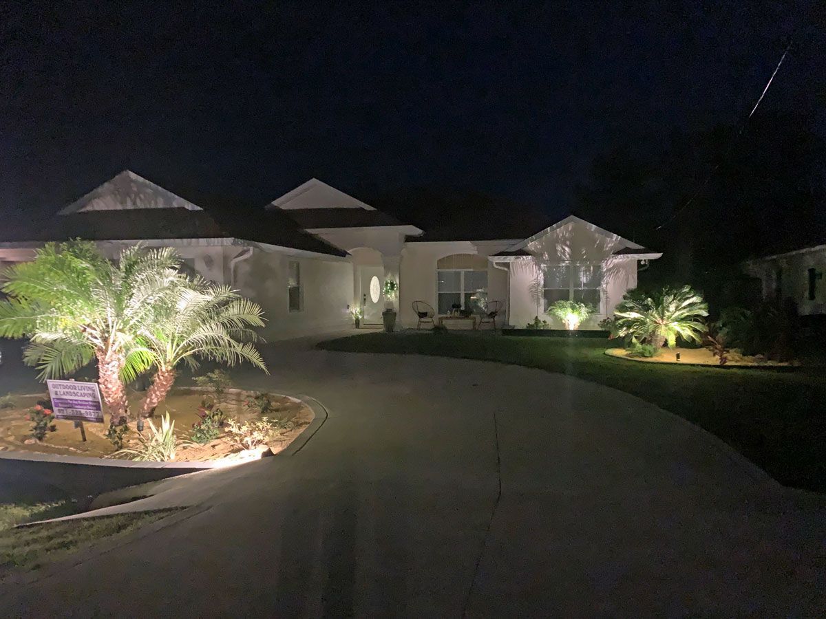 A house is lit up at night with palm trees in front of it.