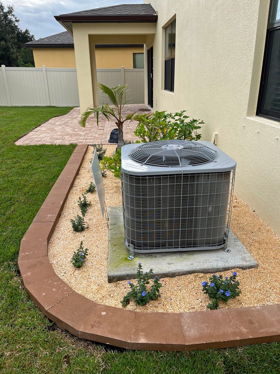An air conditioner is sitting in a garden next to a house.