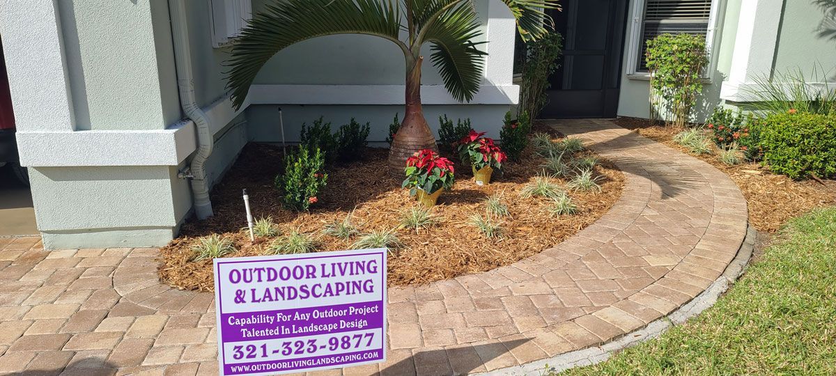 A sign for outdoor living and landscaping is in front of a house.