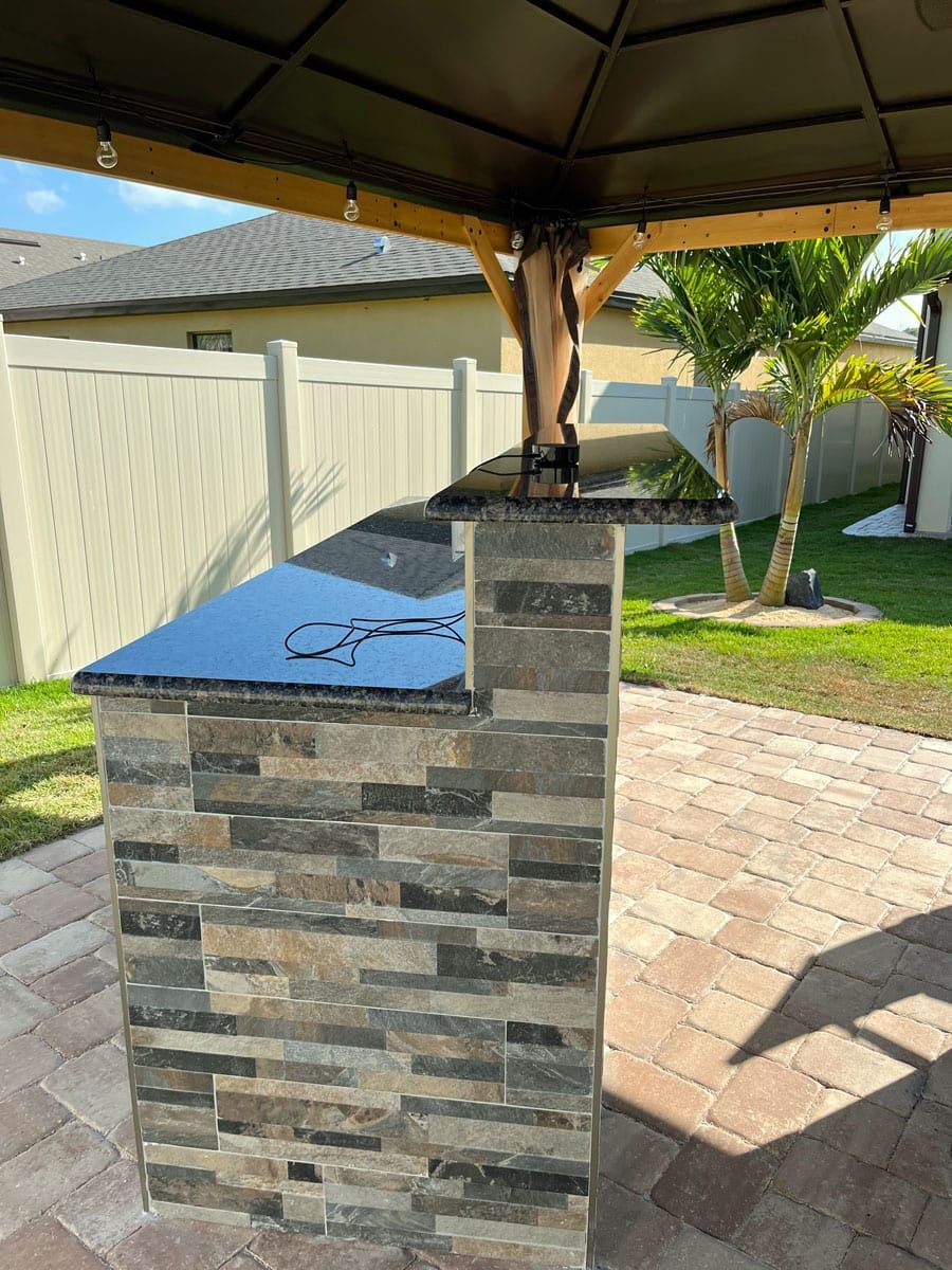 A brick patio with a stone counter top under a gazebo.