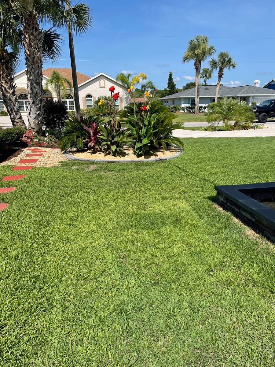 A lush green lawn with flowers and palm trees in front of a house.