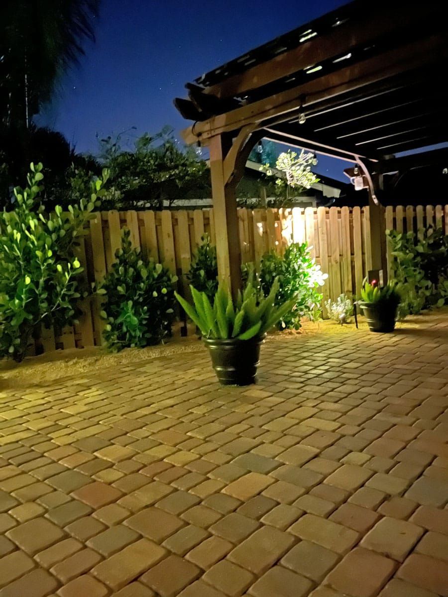 A brick patio with potted plants under a pergola at night.