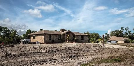 A large house is sitting in the middle of a dirt field.