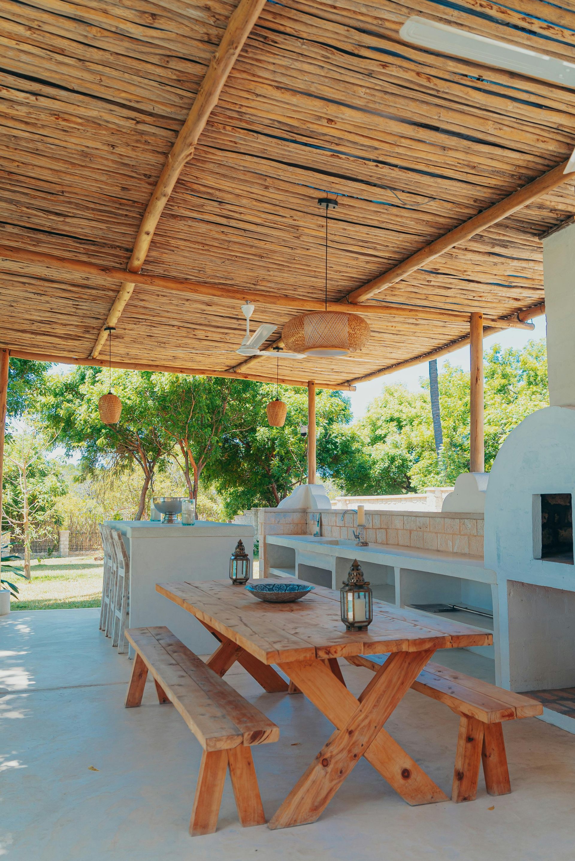 A wooden picnic table with benches under a thatched roof.