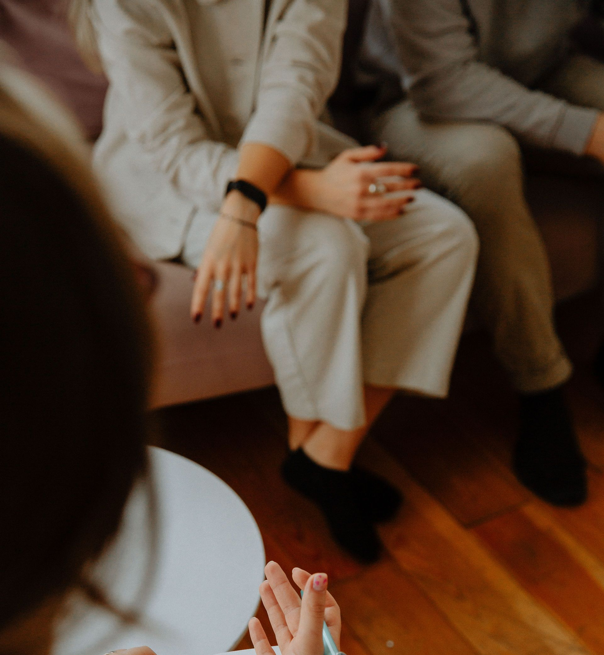 Personas sentadas en el interior, en un sofá, con las manos apoyadas en el regazo durante una reunión grupal