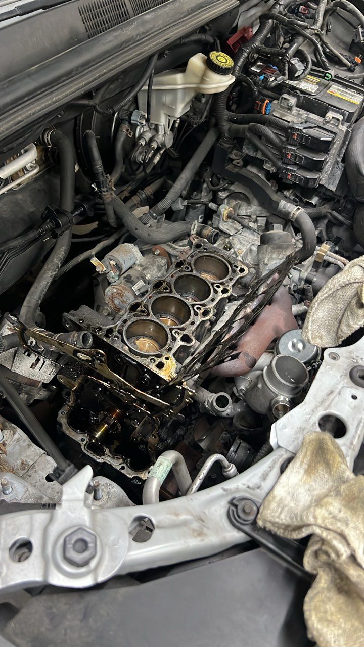 Engine bay with cylinder head removed, exposing pistons and a gasket-covered engine block during repair