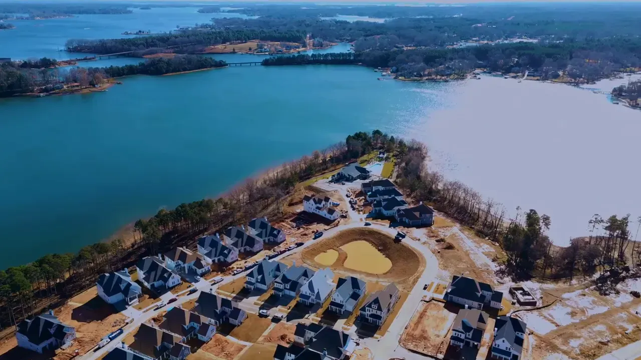 Aerial view of a lakeside neighborhood with houses, roads, and snow-covered ground beside blue water