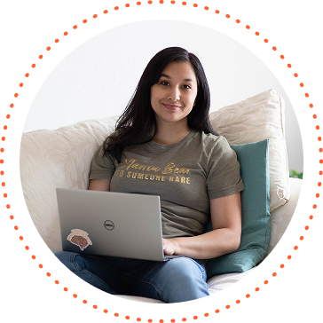 Woman sitting on a couch with a laptop, smiling in a bright room.