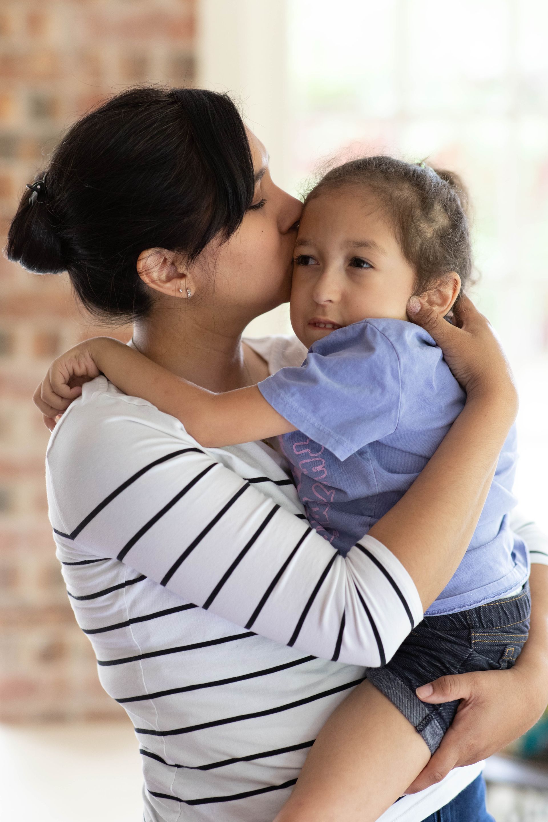 Woman in a striped shirt holding and kissing a young child indoors.