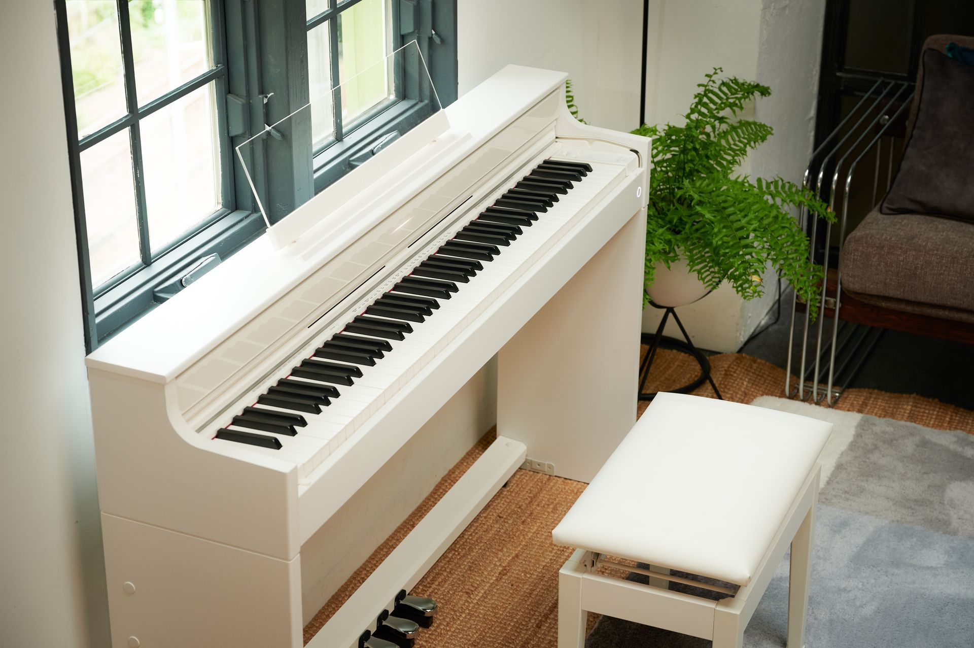 Ein weißes Klavier steht in einem Wohnzimmer neben einem Fenster.